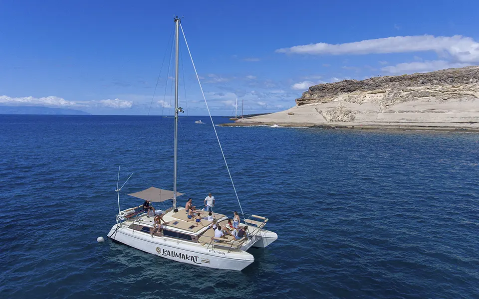 Vista aérea de un catamarán navegando con pasajeros por la costa sur de Tenerife en un día soleado